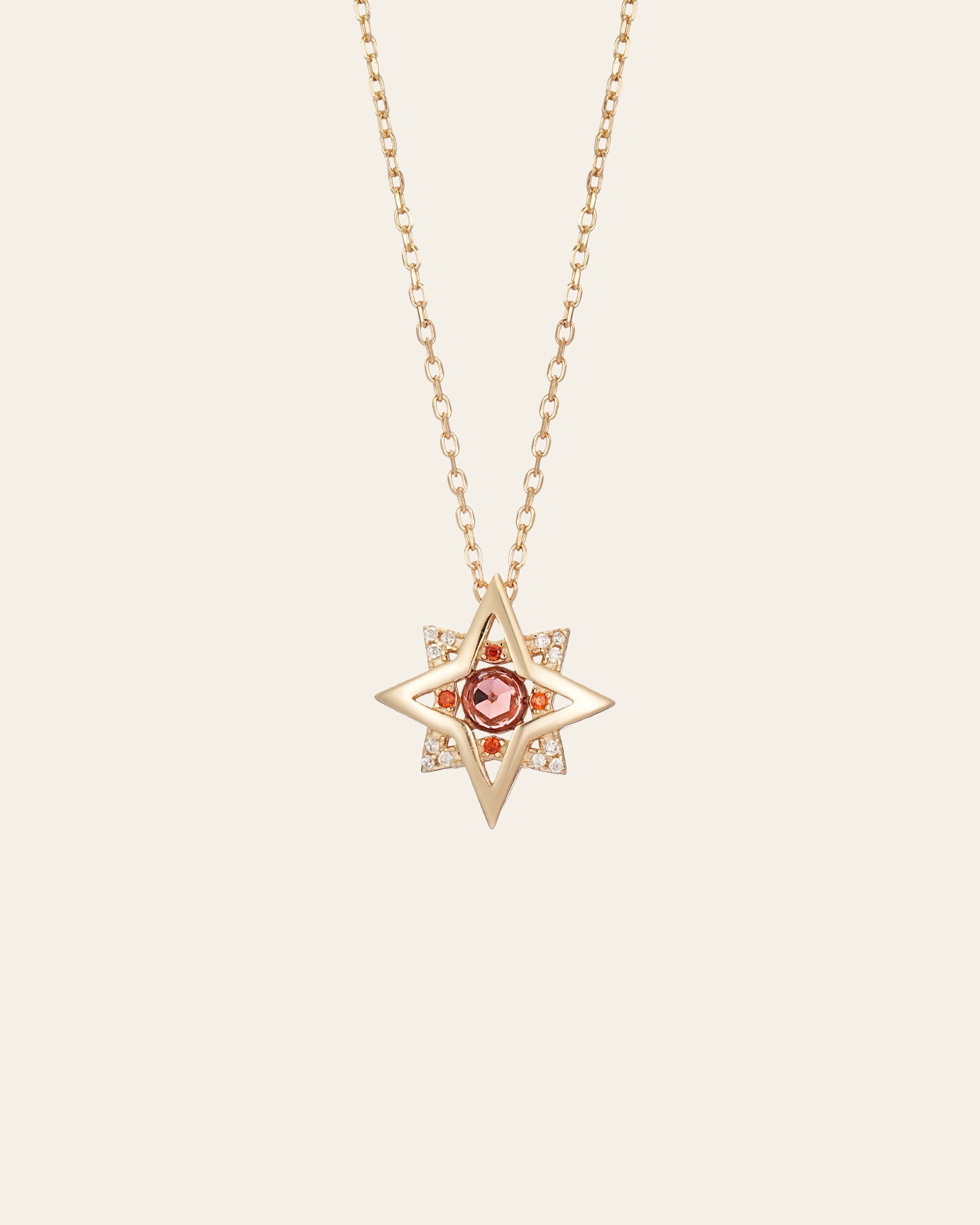 The CAMELLIA New York Garnet Pentagram Necklace is a handcrafted gold star-shaped pendant featuring a central garnet gemstone, encircled by sparkling clear stones on a fine sterling silver chain.