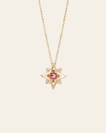The CAMELLIA New York Garnet Pentagram Necklace is a handcrafted gold star-shaped pendant featuring a central garnet gemstone, encircled by sparkling clear stones on a fine sterling silver chain.
