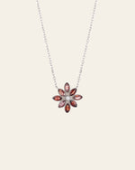 The Cámellia Garnet Pearl Necklace by CAMELLIA features a sterling silver chain with a floral pendant, highlighting garnets and gemstones in pink, red, and white.