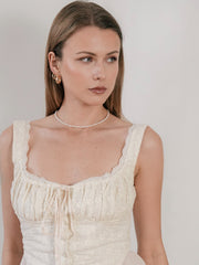 A woman in a cream dress with lace trim and a pearl necklace is enhanced by CAMELLIA Eťa Hoops as she looks to the side against a plain background.